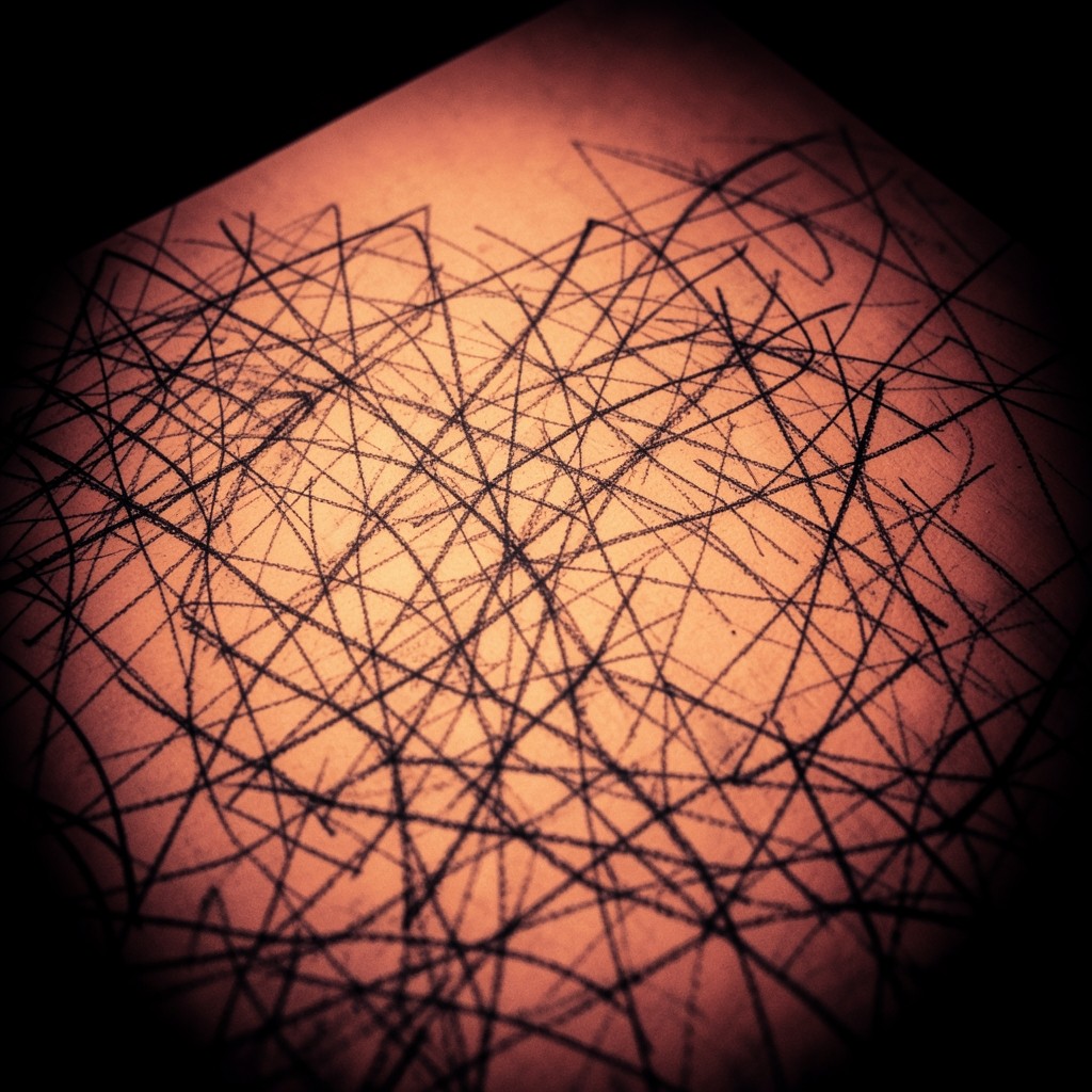 A crowded notebook page of overlapping pencil lines, photographed close under warm low light